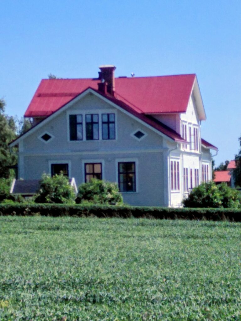 Vitt trähus med rött plåttak, Pilgrimscaféet på Frösön, sett över ett grönt fält. Foto: Marlene Tyckosdotter